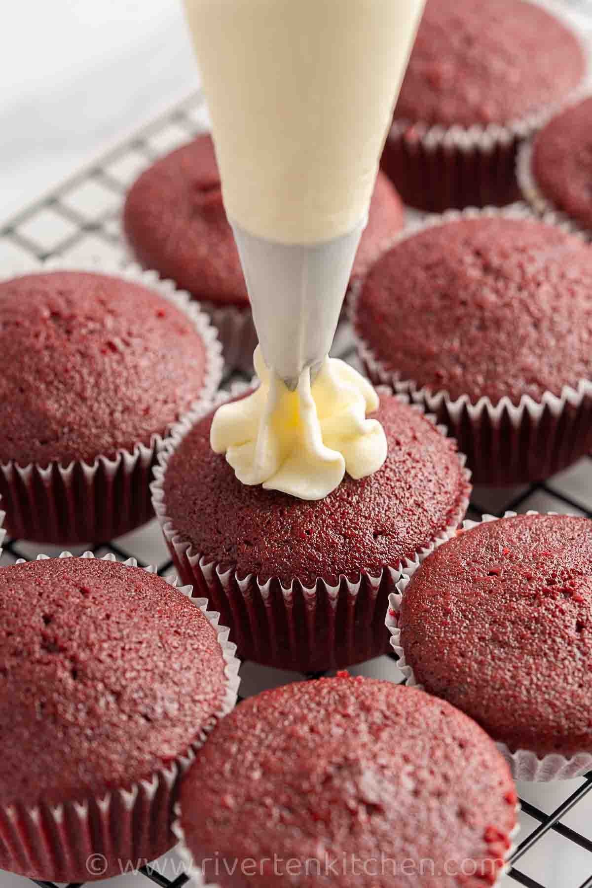 red velvet cupcake being frosted with cream cheese frosting
