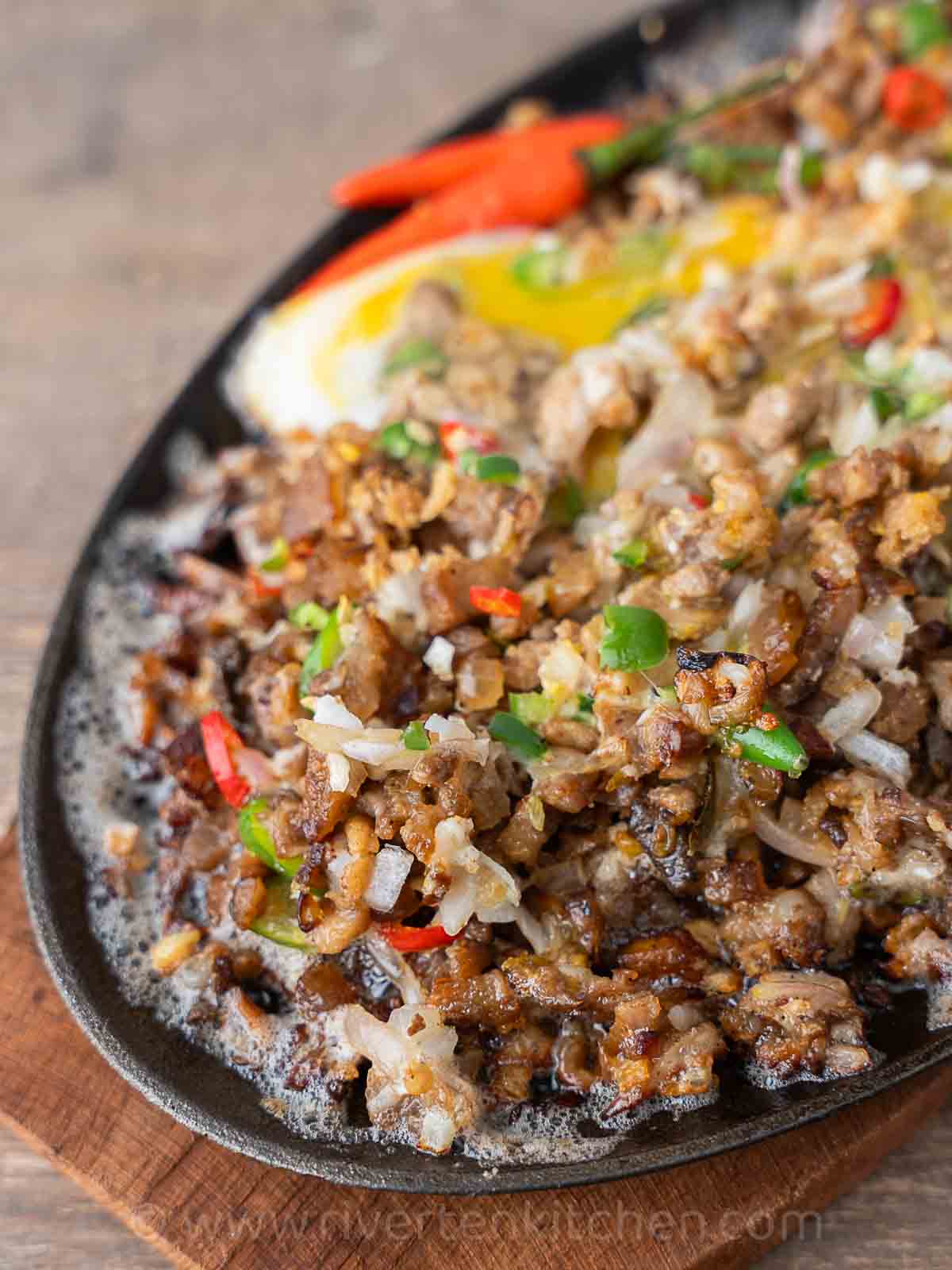 Filipino pork dish called sisig made of pork belly, onions, chilies served on a sizzling plate. Drizzled with calamansi/
