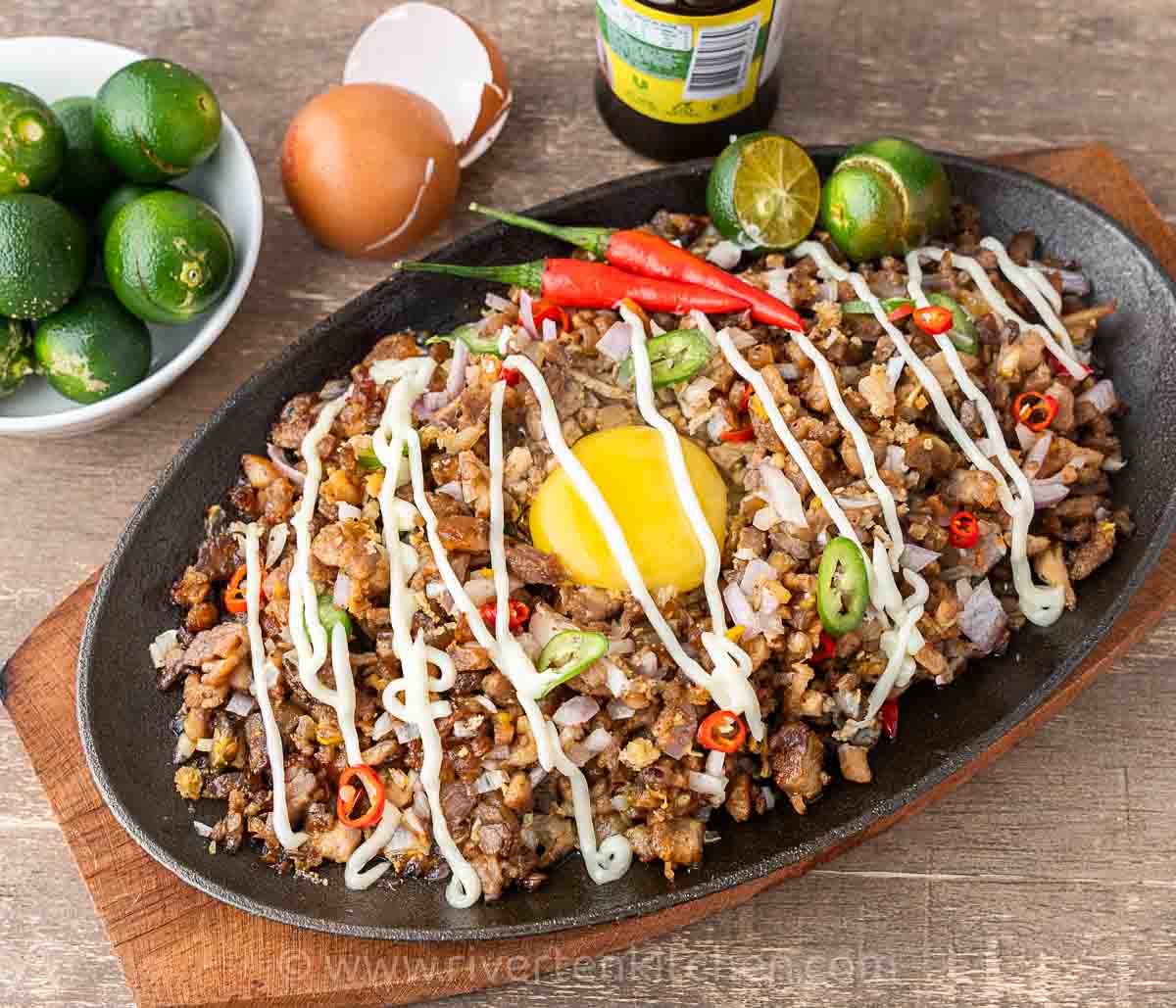 Filipino pork dish called sisig made of pork belly, onions, chilies served on a sizzling plate drizzled with mayonnaise.