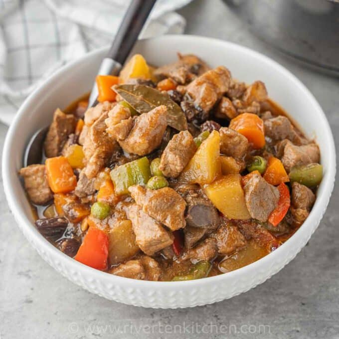Filipino pork and liver stew with carrots and potatoes in a white bowl.