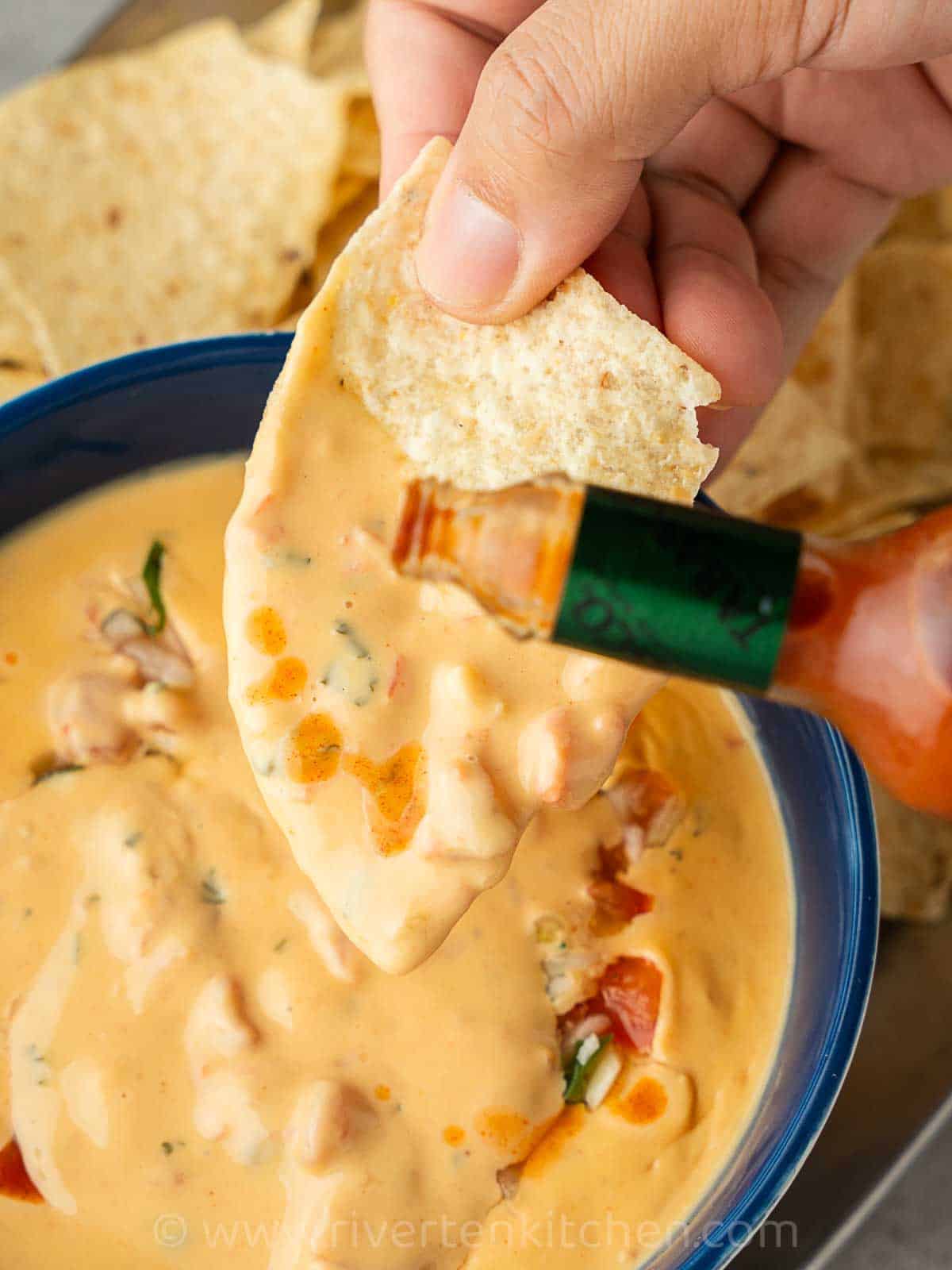 Mexican cheese sauce served on a platter with nachos and tabasco sauce.